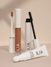 ILIA concealer, mascara, and eye cream set against a neutral background, with applicators visible.
