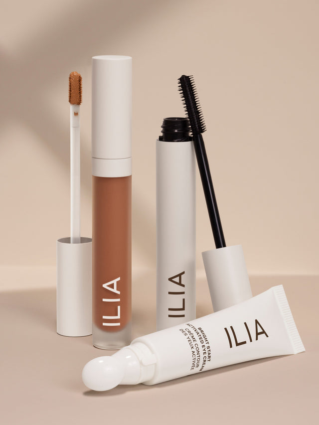 ILIA concealer, mascara, and eye cream set against a neutral background, with applicators visible.