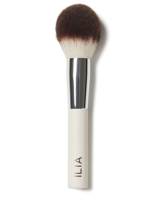 A close-up of the Finishing Powder brush with a white handle and a domed, full-bodied brush.