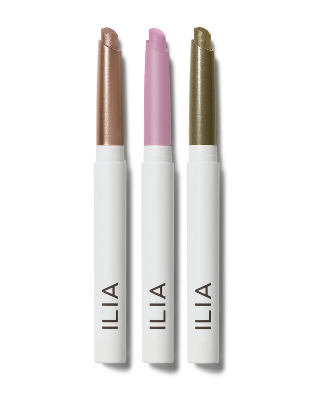 Three ILIA eyeshadow sticks in shimmering and matte shades lined up against a white background.