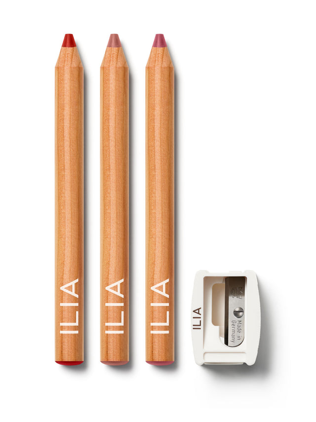 Three ILIA lip liner pencils with a natural wood finish lined up. Featuring an ILIA lip pencil Sharpener placed beside it.