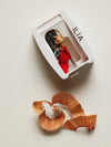 A white ILIA pencil sharpener with a red lip pencil inside, surrounded by shavings.