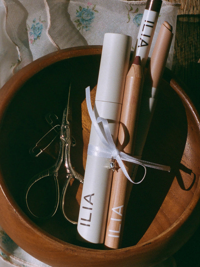 Makeup including a mascara, brown eyeliner, Lip Liner, and Eye shadow tied with an exclusive charm on a wooden surface.