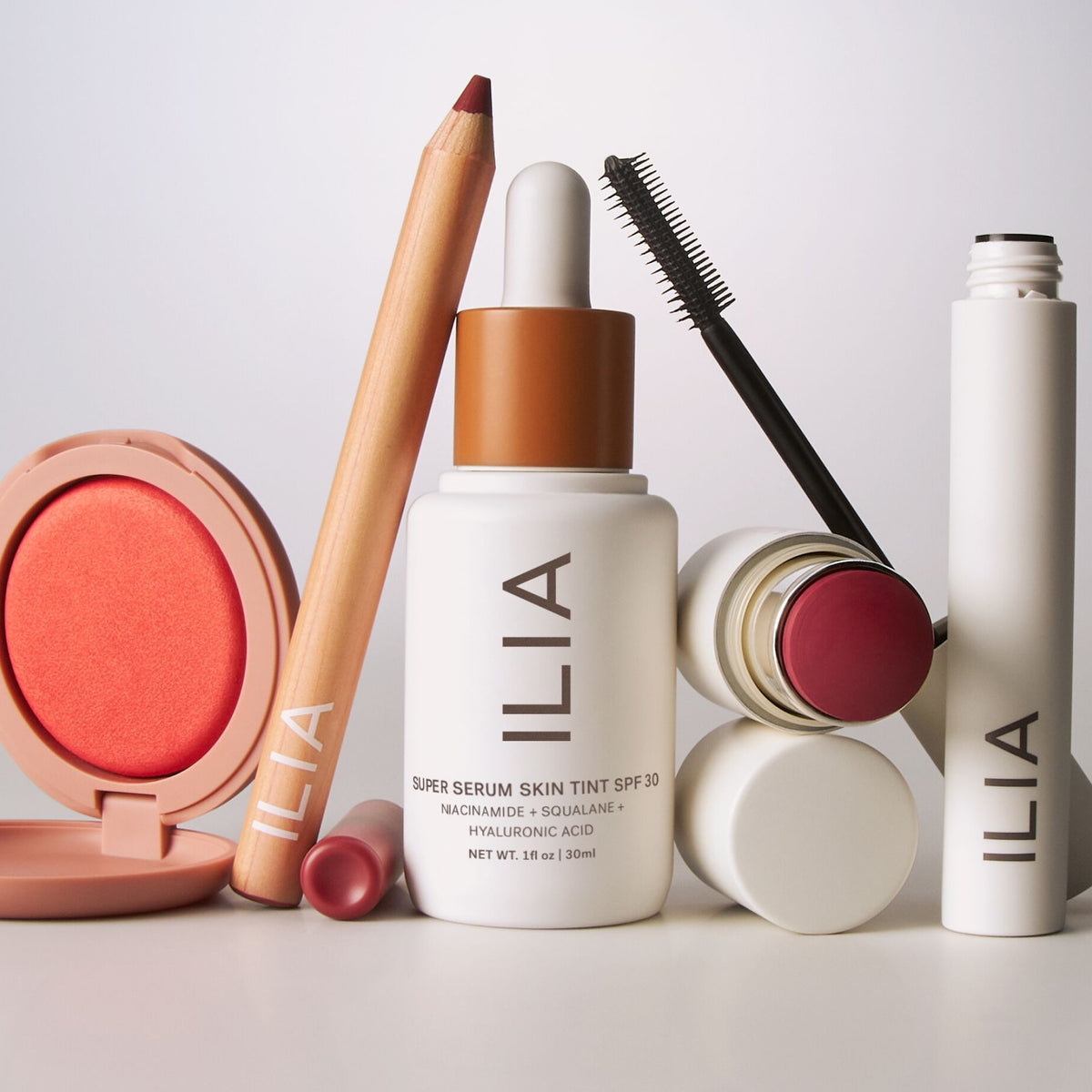 Makeup products including a serum, pencil, and blush with ILIA branding on a light background.