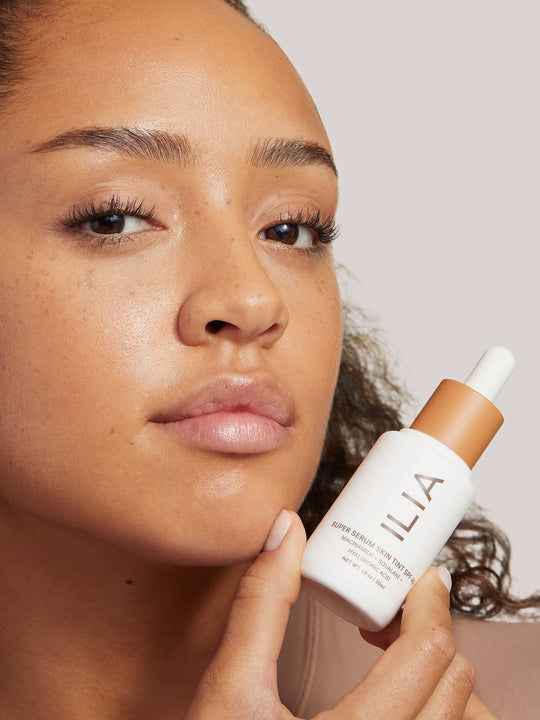 Image of Super Serum Skin Tint bottle next to the dropper applicator. Image includes seals for Allure Best of Beauty Award, Byrdie Eco Beauty Award, and the 1% for the Planet Member