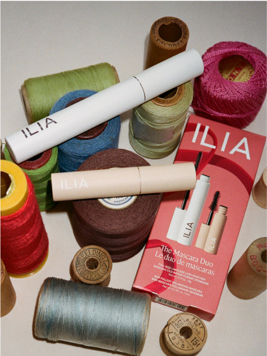Makeup products and spools of thread with 'ILIA' branding on a light background