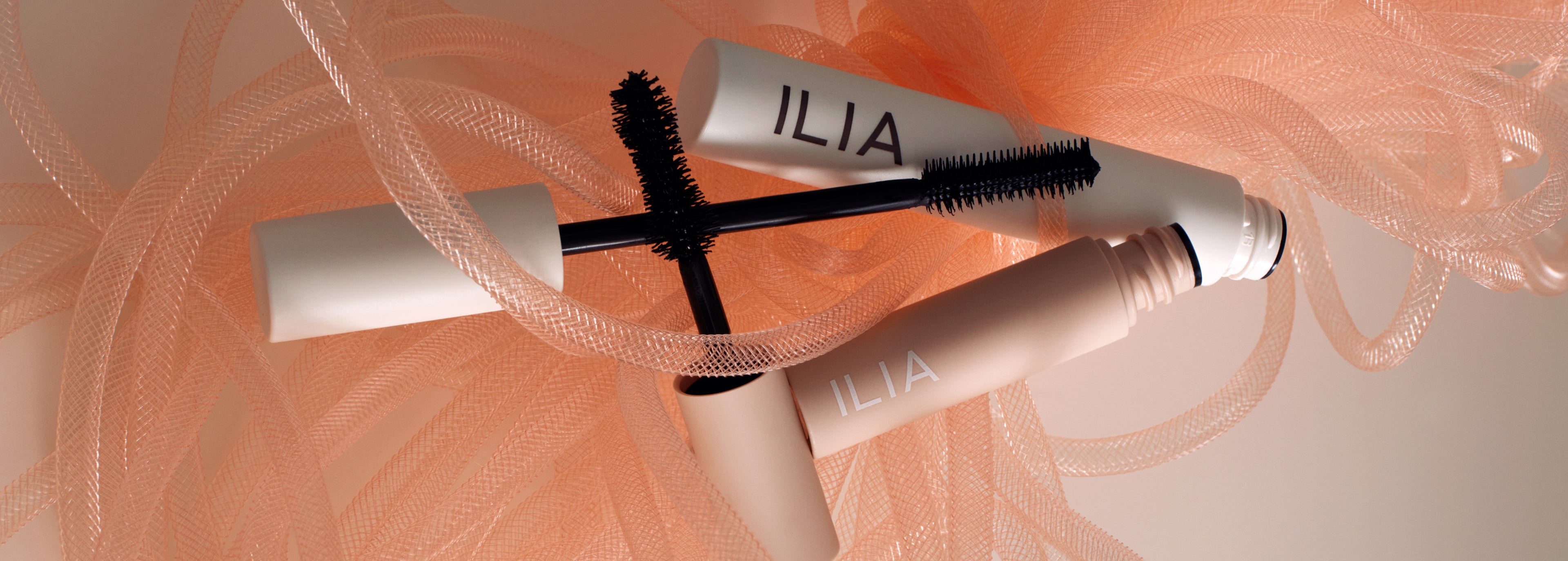 ILIA mascara with brush on a soft peach background