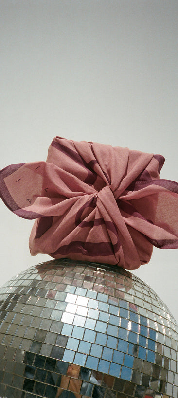ILIA Limited Edition Scarf wrapped around a gift propped on a disco ball against a plain background