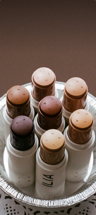 Set of ILIA foundation sticks on a round tray with a brown background