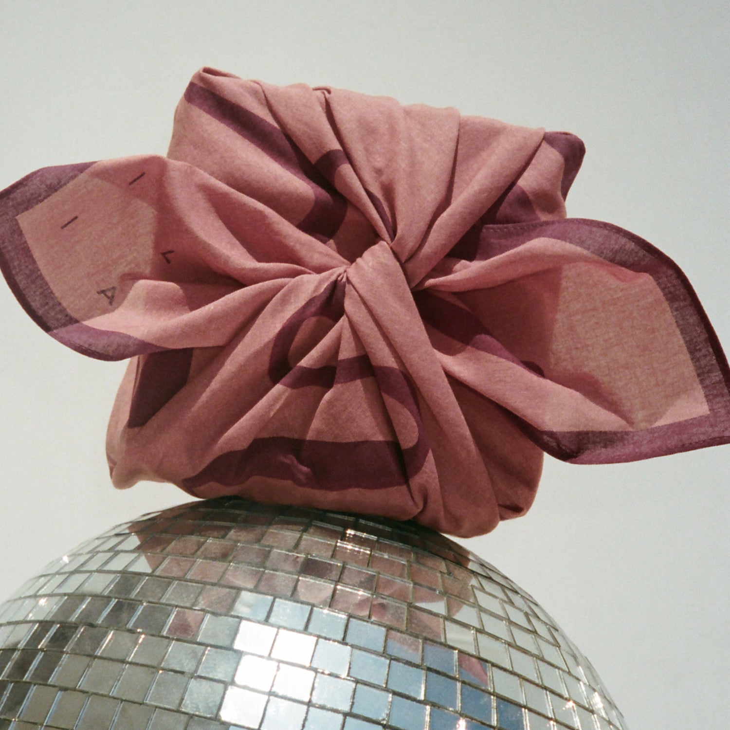 ILIA Limited Edition Scarf wrapped around a gift propped on a disco ball against a light gray background